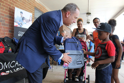 A student receives a backpack with school supplies from Comcast Spotlight Regional Vice President Michael Miller.