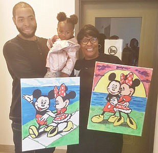 Artist Will Brown holding two-year-old  Ta’liya Fleming, who has lost three godbrothers to gun violence. She loves Mickey and Minnie Mouse. Millie Brown holds the paintings her son created for her.