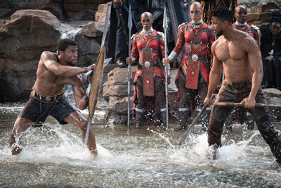 T'Challa/Black Panther (Chadwick Boseman) and Erik Killmonger (Michael B. Jordan) fight as female warriors known as Dora Milaje who protect the king  look on. 